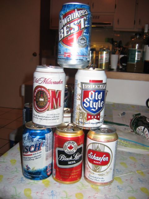 1985 Ford LTD Crown Victoria - A pyramid of assorted beer cans is stacked on a table, with a kitchen counter visible in the background.