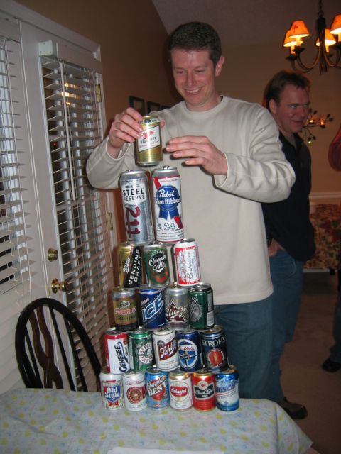 1985 Ford LTD Crown Victoria - A pyramid of beer cans is being built by a man, with another person watching.