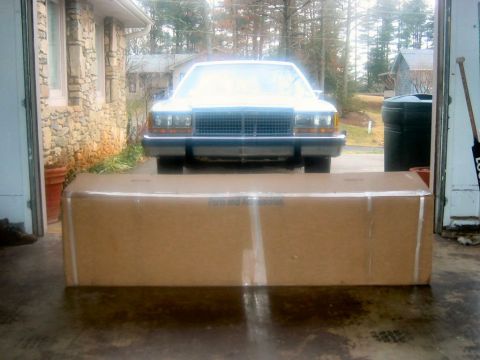 1985 Ford LTD Crown Victoria - A white sedan from the 1980s is parked in a garage, partially obscured by a large cardboard box.