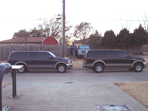 Two black Ford Excursion SUVs parked nose-to-nose on a residential street at dusk