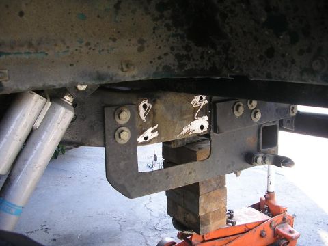 1979 Chevrolet C/K Pickup - The underside of a truck, focusing on the frame, shocks, and a hitch receiver, is elevated for work.