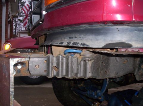 1995 Ford Bronco - Low-angle close-up under the front of a maroon truck showing the bare frame horns with a freshly welded steel bumper mount bracket bolted o…