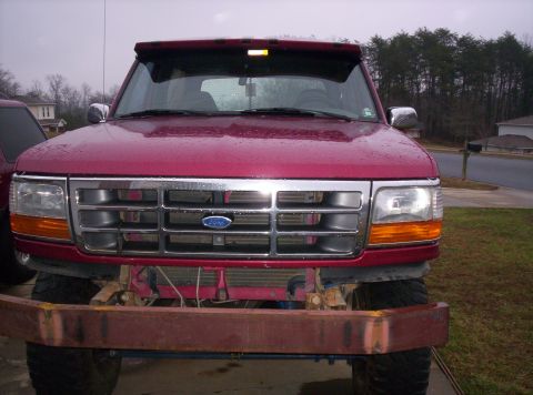 1995 Ford Bronco - Head-on view of a rain-beaded maroon 1992-96 Ford truck with the factory bumper and valance removed, showing a bare rusty channel-steel bea…
