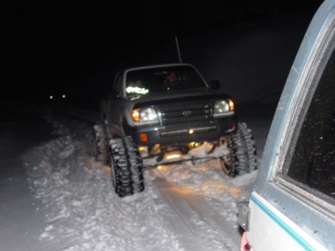 1986 Ford Bronco - A Toyota Tacoma equipped with tracks navigates a snowy path in the dark.