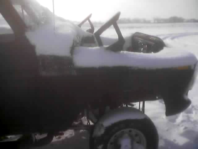 Dark vehicle with snow on hood and roof, side view, with a wheel visible in snow