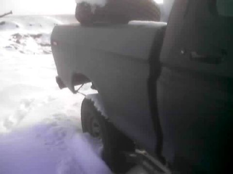 1979 Ford Bronco - A dark colored truck is partially buried in snow, showing its rear quarter panel and wheel.
