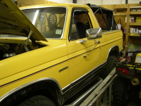 1982 Ford Bronco - Yellow Ford Bronco with black trim and a soft top, hood open, on a ramp.