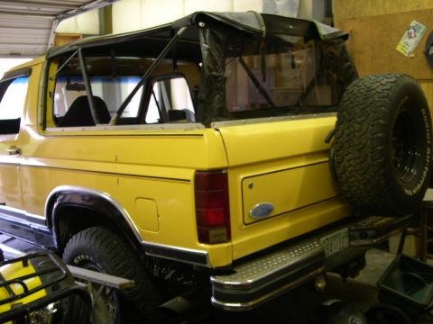 1982 Ford Bronco - Rear view of a yellow 1982 Ford Bronco a soft top and a spare tire mounted on the back.