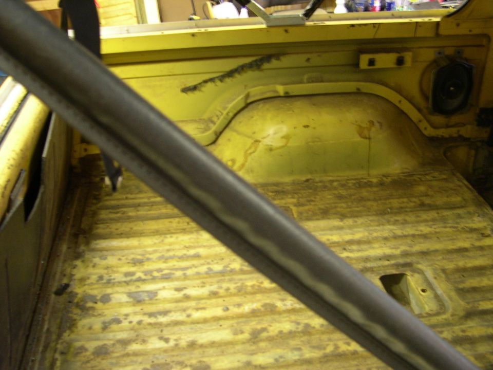 Interior of a yellow vehicle, showing the floor and rear seating area with a roll bar in the foreground
