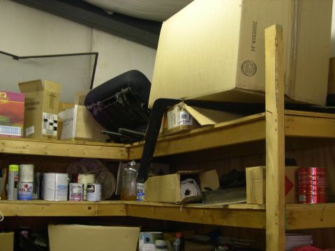 1982 Ford Bronco - Shelving unit filled with various items including boxes, paint cans, and a chair, suggesting a storage area.
