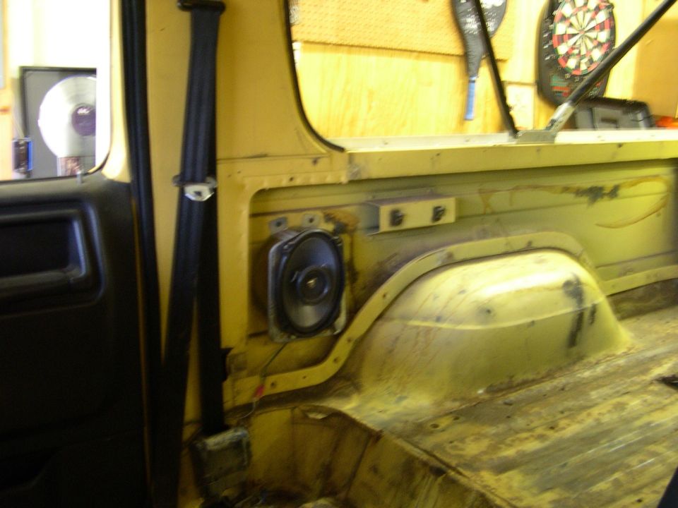 Interior shot of a yellow vehicle showing a speaker mounted on the side panel, a seatbelt, and the rear cargo area