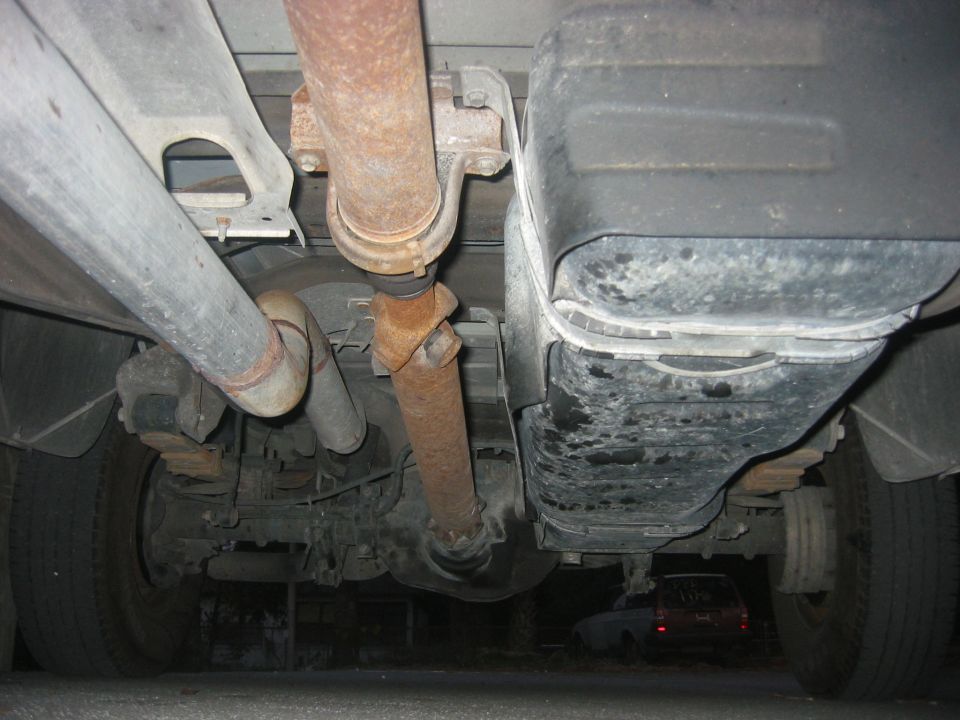 Underside view of vehicle with exhaust pipes, driveshaft, and fuel tank visible