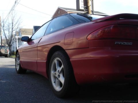 1996 Ford Probe - Rear quarter view of a red 1996 Ford Probe coupe parked on a street, with a dark SUV visible in the distance.