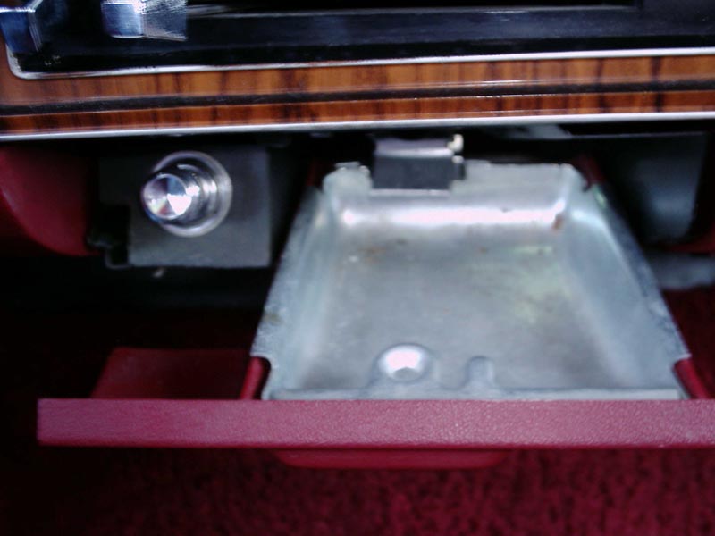 Cleaned-out metal dash ashtray open on a red interior with woodgrain dash trim