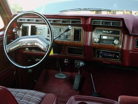 1984 Ford Bronco - The interior of a vehicle features a wood-grain dashboard, a Ford steering wheel, and an XLT radio.