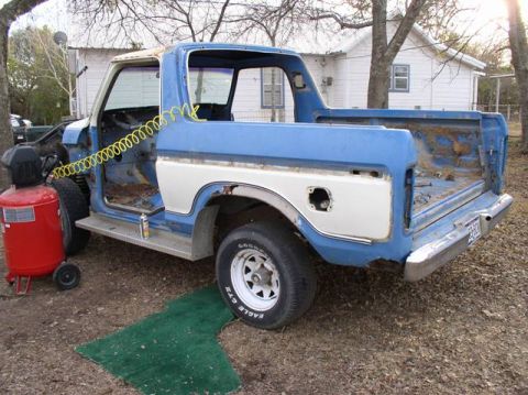 1978 Ford Bronco - A blue and white Ford Bronco body is undergoing restoration, with its doors removed and an air compressor nearby.