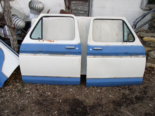 Two white and blue car doors with rust spots and visible door handles