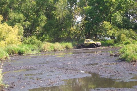 1985 Toyota T100 - A yellow pickup truck is stuck in a muddy area surrounded by trees and tall grass.