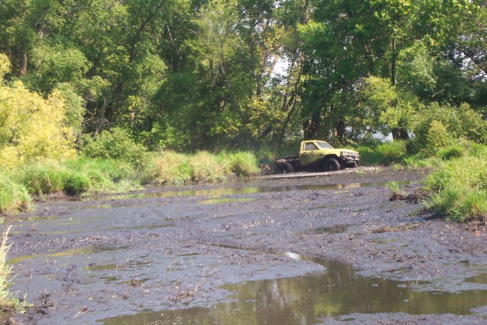 Yellow compact pickup with stripped bed at the edge of a large mud bog