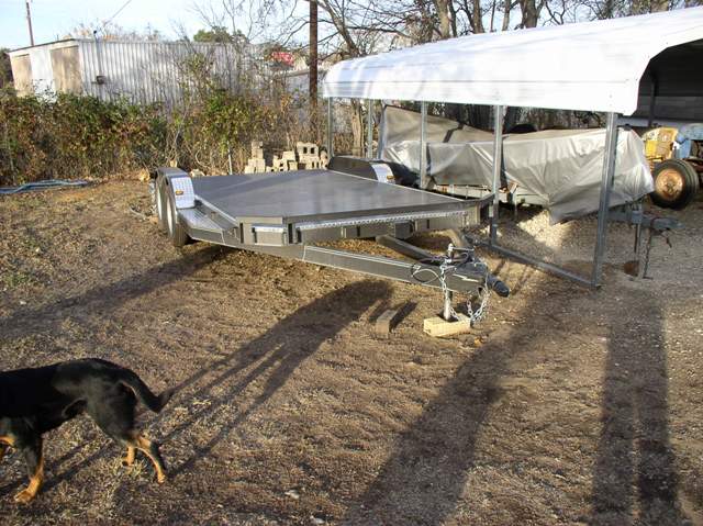car hauler trailer parked on dirt, dog in foreground, other vehicles covered in background