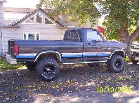 1985 Ford F-150 - This 1985 Ford F-150 pickup truck is shown from the side, its distinctive 4x4 badging and racing stripes.