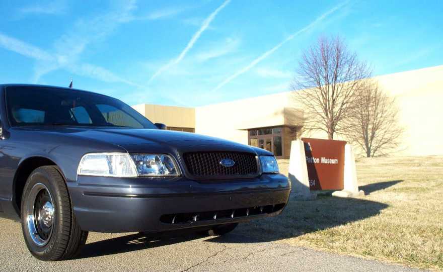 Dark Ford Crown Victoria with blacked-out grille parked by a Patton Museum sign