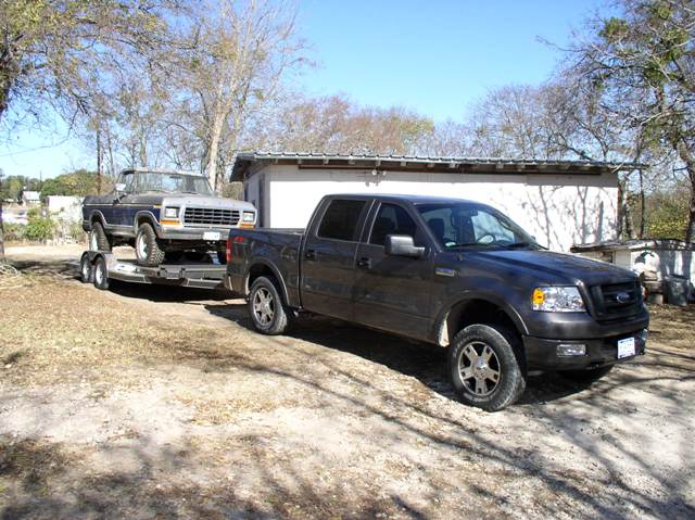 Dark gray Ford F-150 pickup truck towing a blue and silver Ford Bronco on a trailer