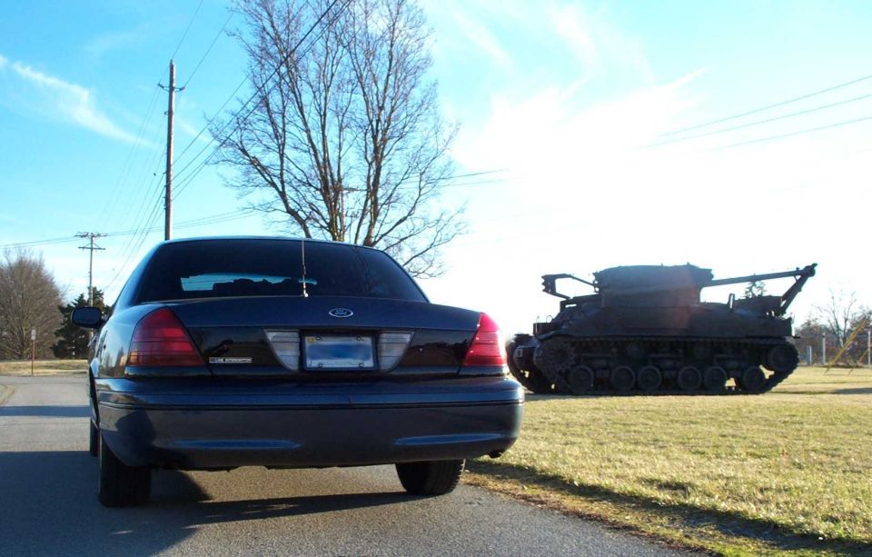 Rear view of a dark blue Ford Crown Victoria Police Interceptor beside a display tank