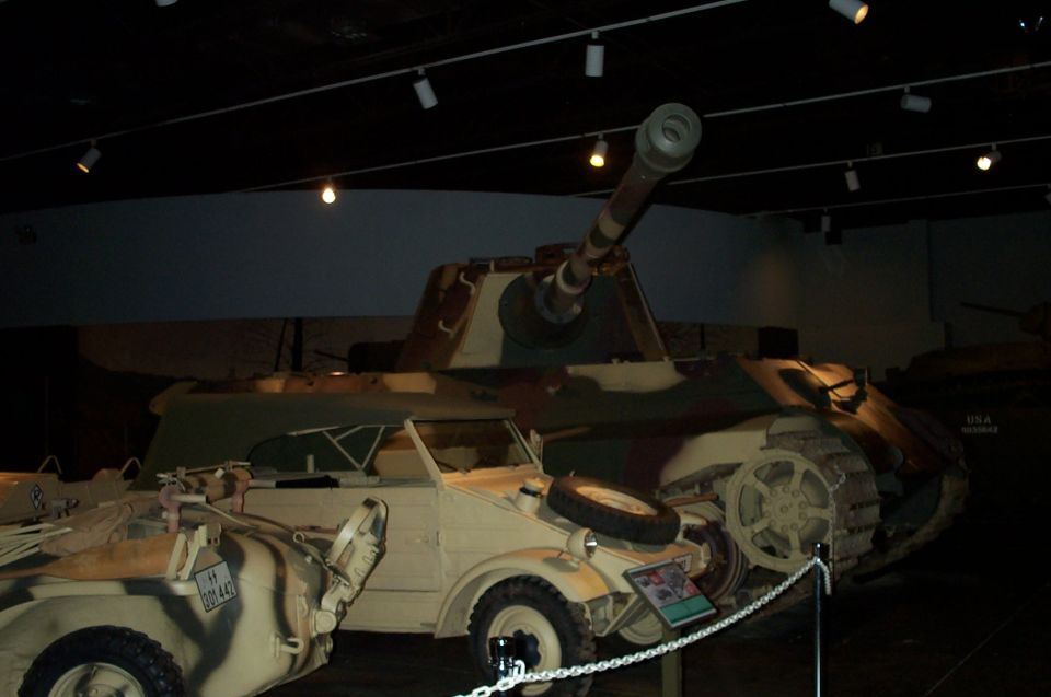 Camouflage-painted tracked tank and small military car on display in dim museum hall