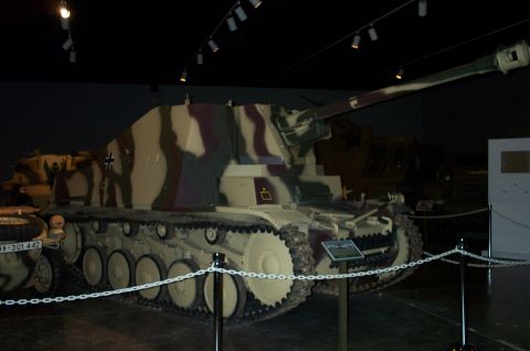 1998 Ford Crown Victoria - A camouflaged tank is displayed indoors, with another vehicle partially visible to the left.