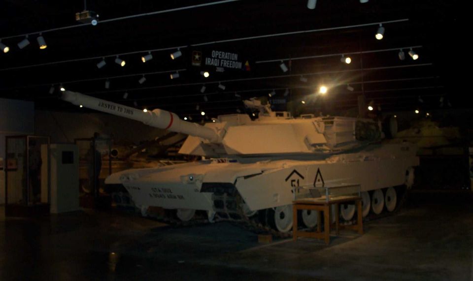 Tan M1 Abrams tank on display in a museum under an Operation Iraqi Freedom banner