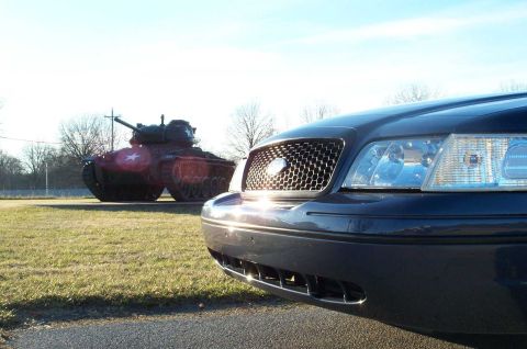 1998 Ford Crown Victoria - A dark blue 2003 Ford Crown Victoria is parked on asphalt, with a military tank visible in the grassy field behind it.