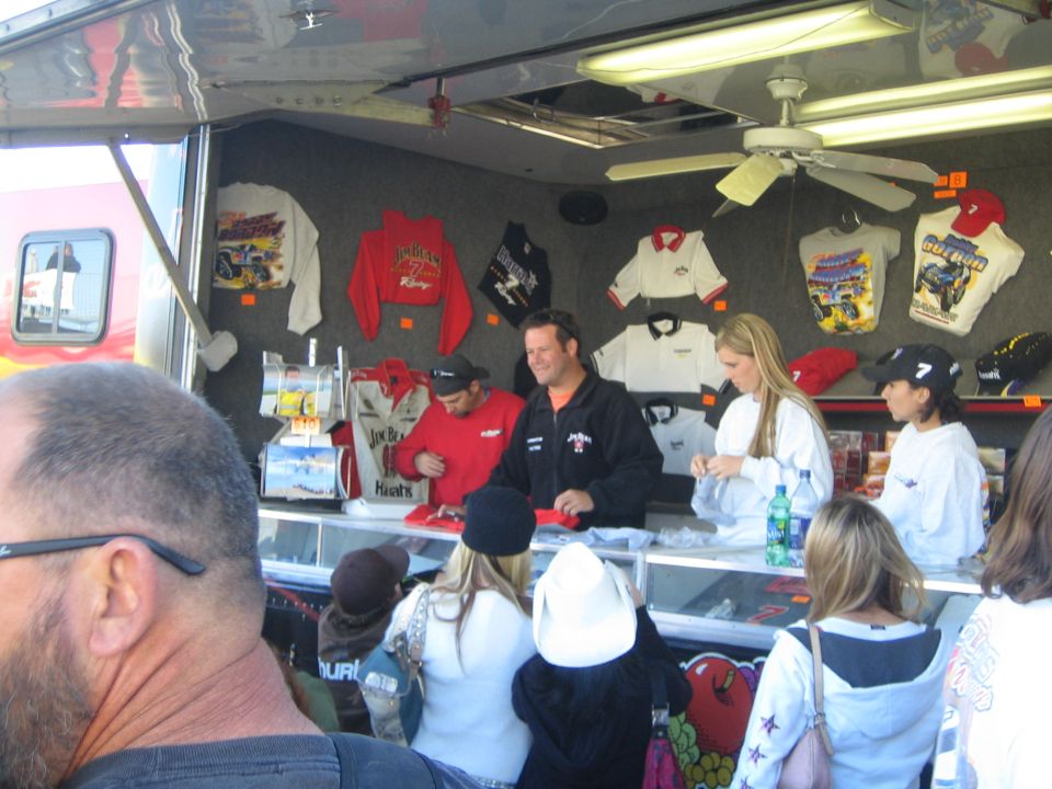 People at a merchandise trailer counter with hanging shirts and hats