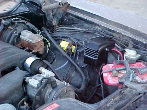1973 Ford Ranchero - Engine bay view showing a dirty, worn engine compartment with a black finned voltage regulator or coil box mounted centrally, a yellow conn…