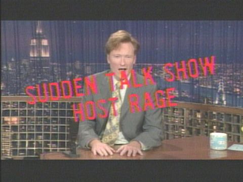 2000 Ford Crown Victoria - A talk show host appears on set with a city skyline in the background and superimposed text.