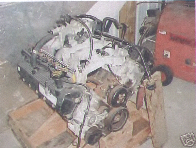 V8 engine assembly with hoses and belts, resting on a wooden stand