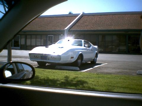 2000 Mercury Grand Marquis - A white classic car with custom bodywork is parked in a lot, viewed through the window of another car.