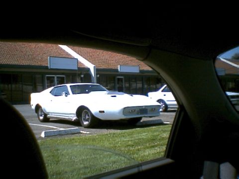 2000 Mercury Grand Marquis - A white coupe with a hood scoop is parked in a lot next to another white vehicle.