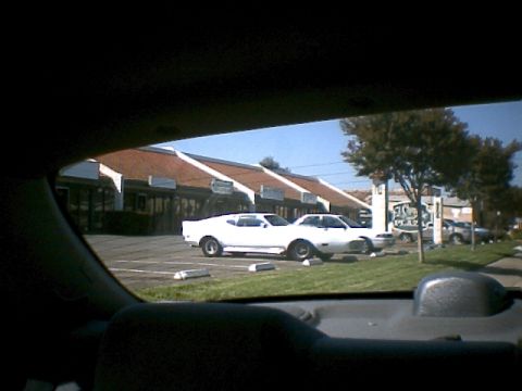 2000 Mercury Grand Marquis - Two white coupes are parked in a lot in front of a strip mall.