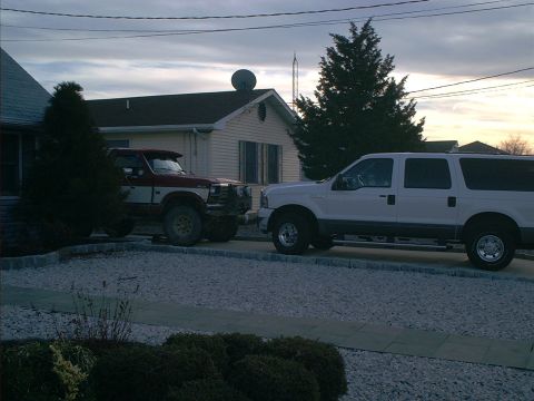 2005 Ford Excursion - Two Ford trucks are parked in a driveway in front of a house during the day.
