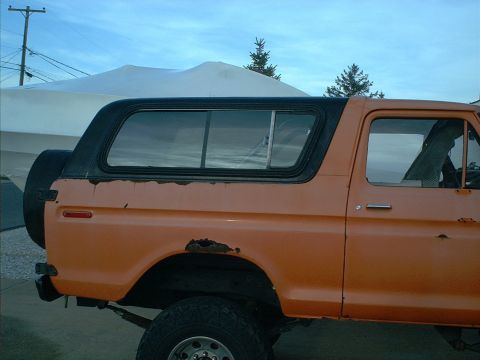 1978 Ford Bronco - The side profile of an orange 1978 Ford Bronco shows significant rust damage on the rear quarter panel.