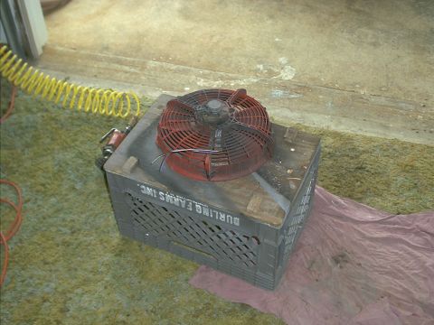 1978 Ford Bronco - A red radiator fan is placed on a plastic crate, with an air hose nearby.