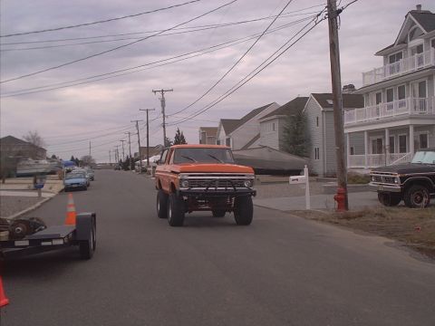 1978 Ford Bronco - Orange 1978 Ford Bronco driving on a street with houses and a black Bronco parked nearby.