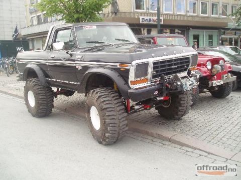 1979 Ford Bronco - Modified black Ford Bronco with massive tires and a front-mounted winch, seen alongside other vehicles.