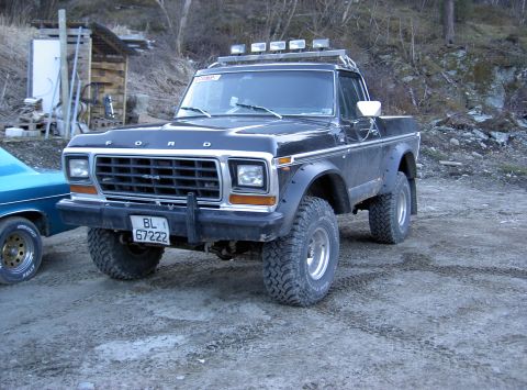 1979 Ford Bronco - Black 1979 Ford Bronco with off-road tires and roof lights sits on a dirt lot next to another car.