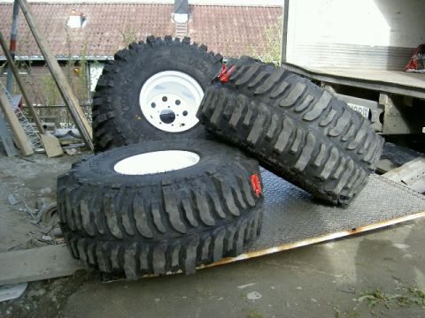 1979 Ford Bronco - Several large off-road tires are positioned on a ramp, with a building and truck in the background.