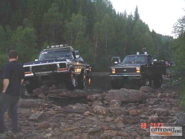 Two lifted dark 4x4 trucks parked on a rocky riverbed at dusk