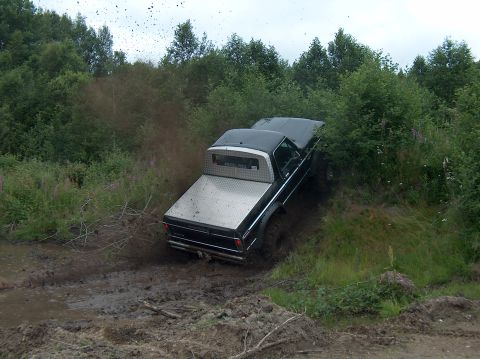 1979 Ford Bronco - Pickup truck struggling through a muddy off-road course with trees and vegetation on the sides.