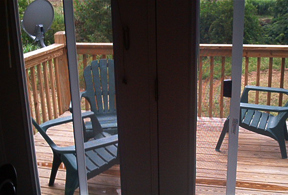 Deck with two green plastic chairs, wooden railing, and a satellite dish