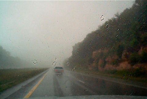 1985 Ford LTD Crown Victoria - A car travels down a wet highway during a rainstorm, with water droplets obscuring the view through the windshield.
